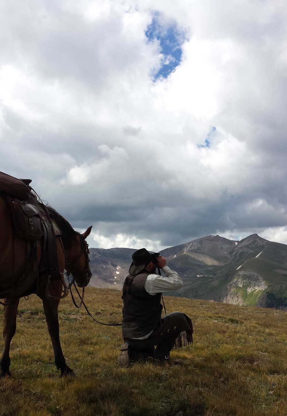 Hunter glassing for elk from a mountain ridge with a heavy pack at dawn