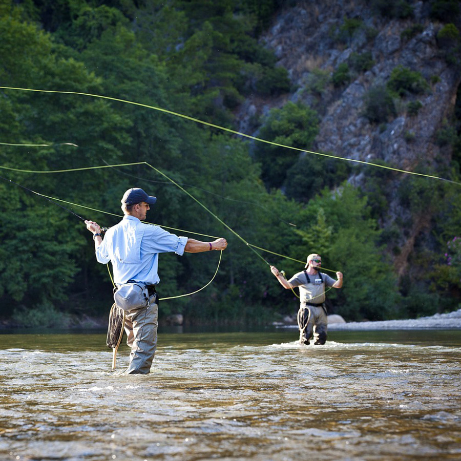 Beginner fly angler casting on a calm river with mountains in the background