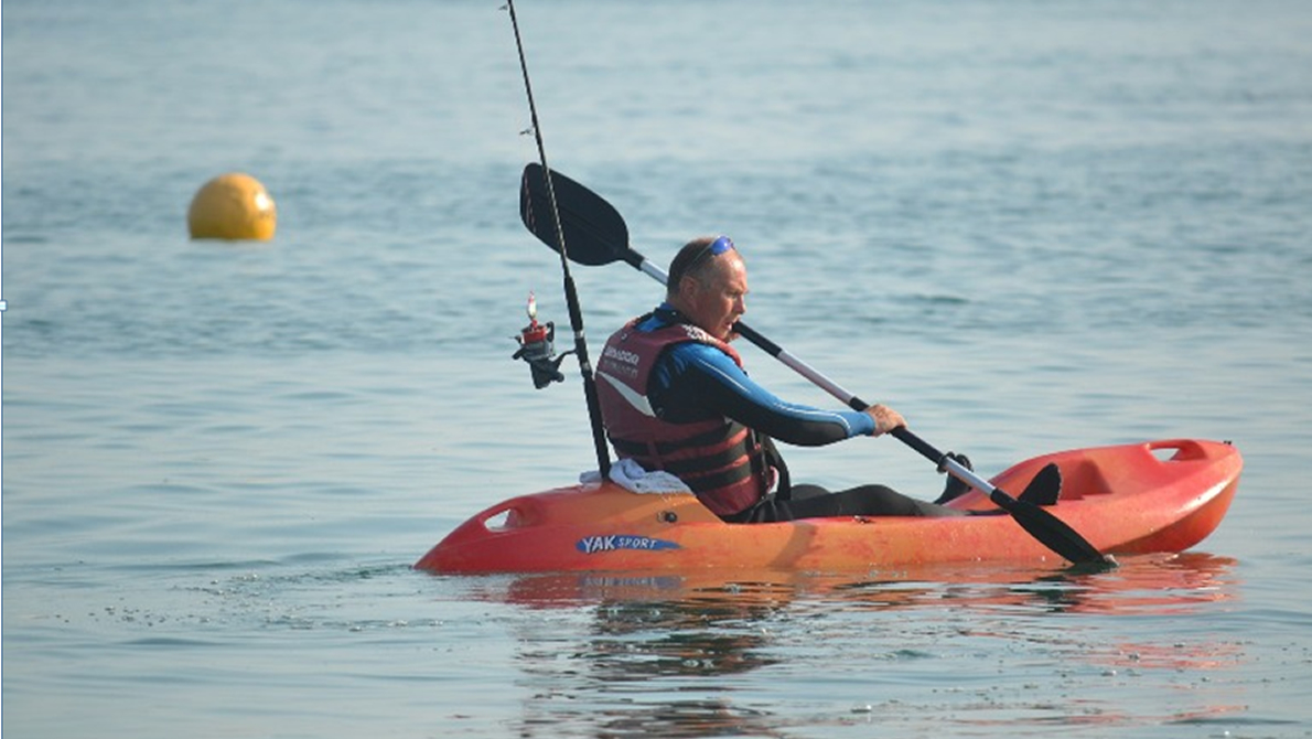Beginner angler casting from a sit-on-top fishing kayak on a calm protected bay at sunrise